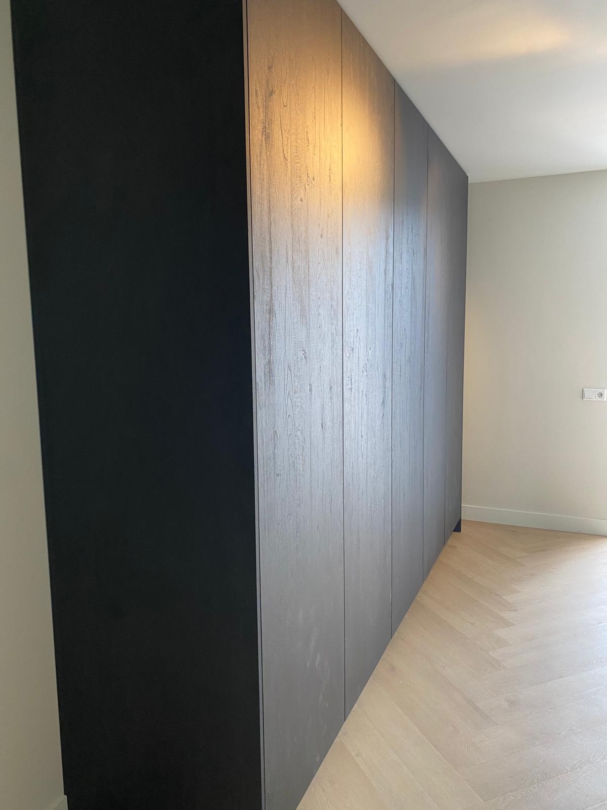 Maatwerk kastenwand met donkere houtstructuur tot aan het plafond