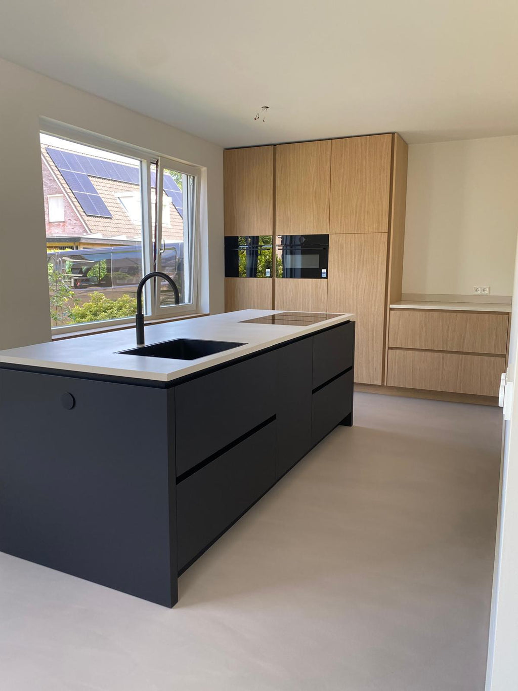Maatwerk keuken met zwart kookeiland en lichte houten kastenwand
