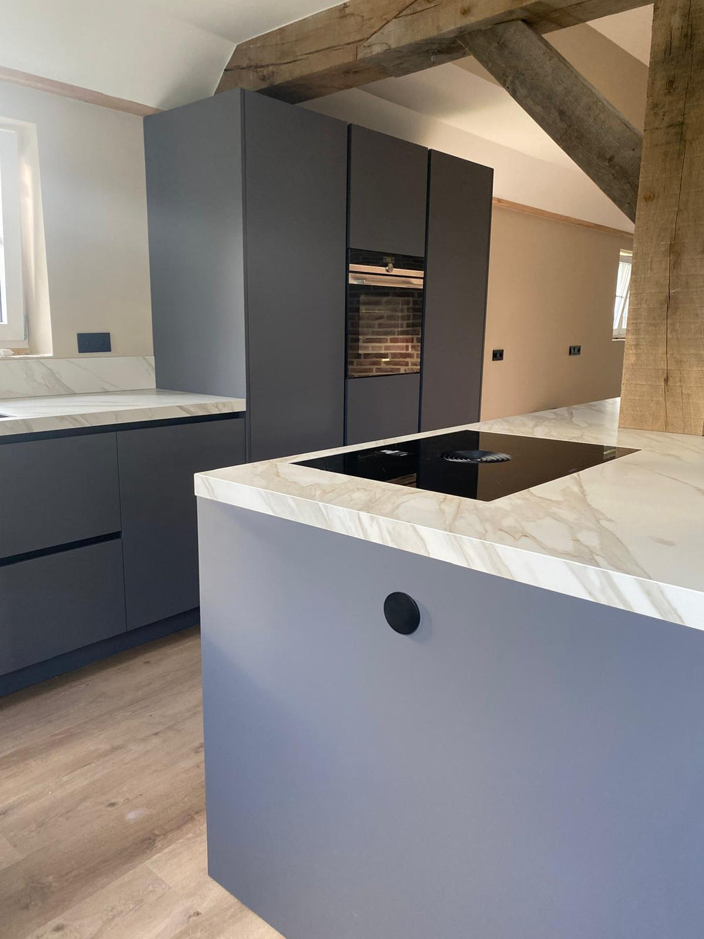 Donkergrijze maatwerk keuken met kookeiland en houten balkconstructie