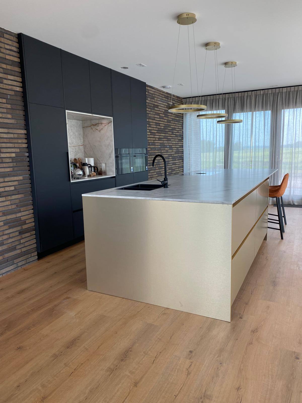 Luxe maatwerk keuken met goudkleurig kookeiland en donkere kastenwand
