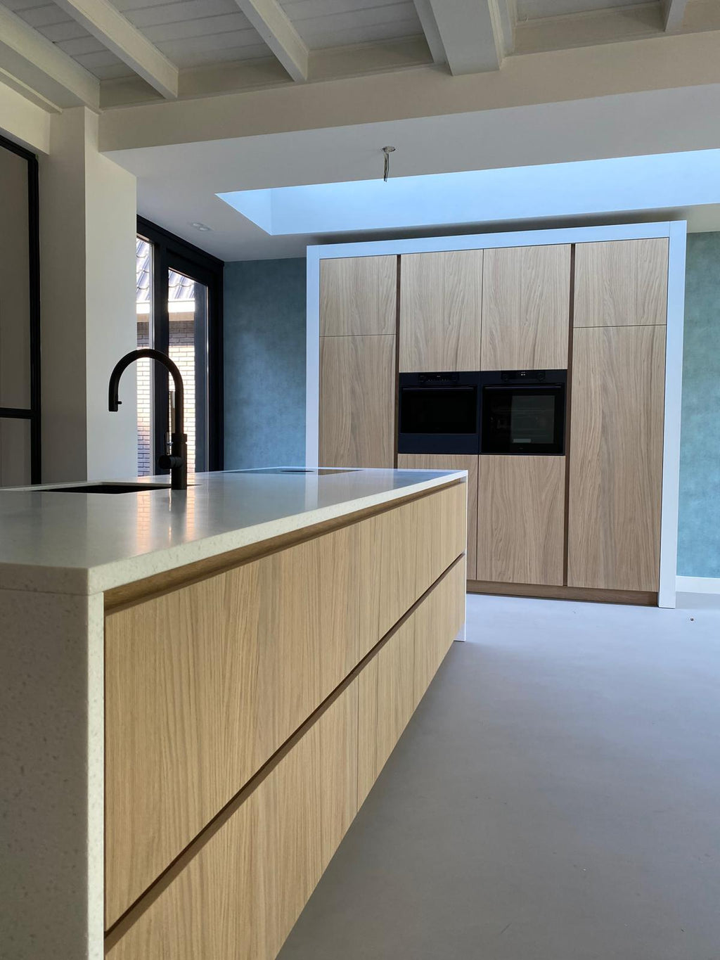 Maatwerk keuken met houten kookeiland, licht werkblad en hoge kastenwand
